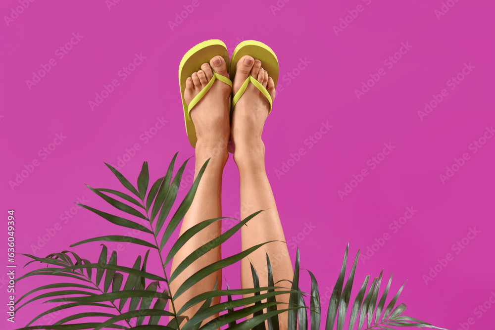 Legs of young woman in flip-flops and tropical leaves on magenta background