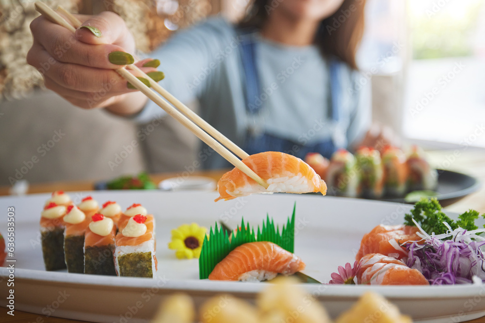 Hands, chopsticks and woman with sushi in restaurant, fine dining and eating in cafe store. Salmon, 