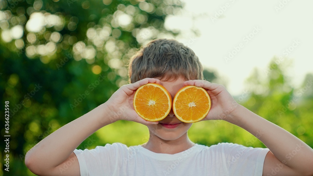 Cute child is holding orange slices like orange glasses. Boy child plays with fresh juicy oranges. C