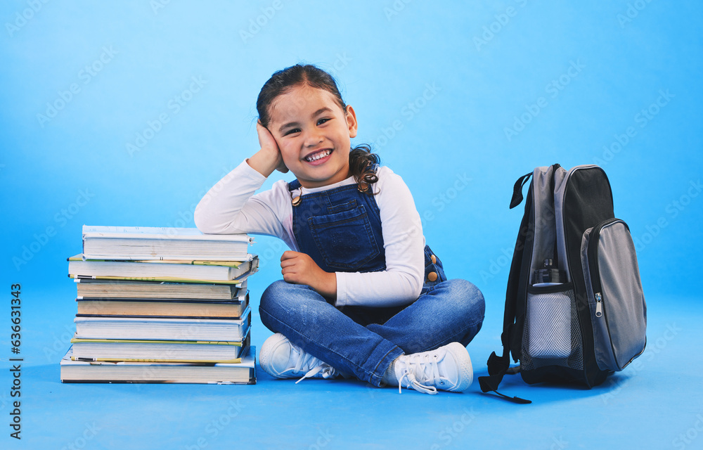 Girl child, sitting and books in studio portrait, backpack and excited for learning on floor by blue