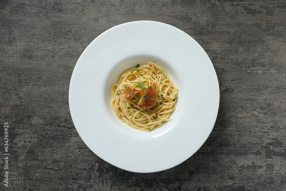 Tasty spaghetti with prosciutto and microgreens on grey textured table, top view. Exquisite presenta