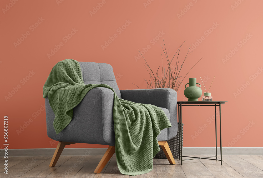 Grey armchair with green plaid and table near color wall in room