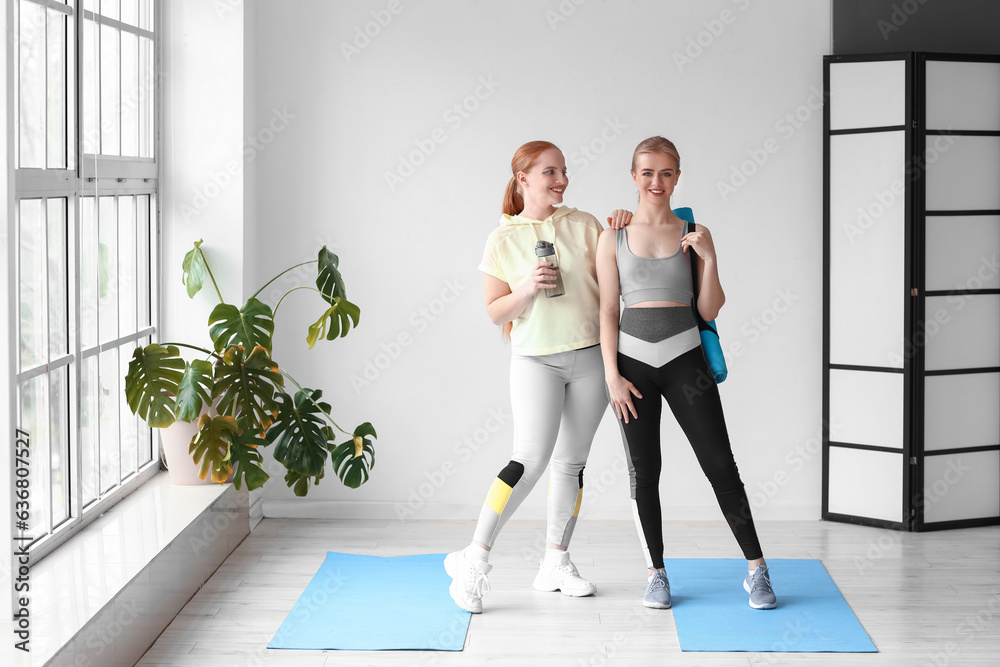 Portrait of sporty young women with bottle of water and yoga mat in gym