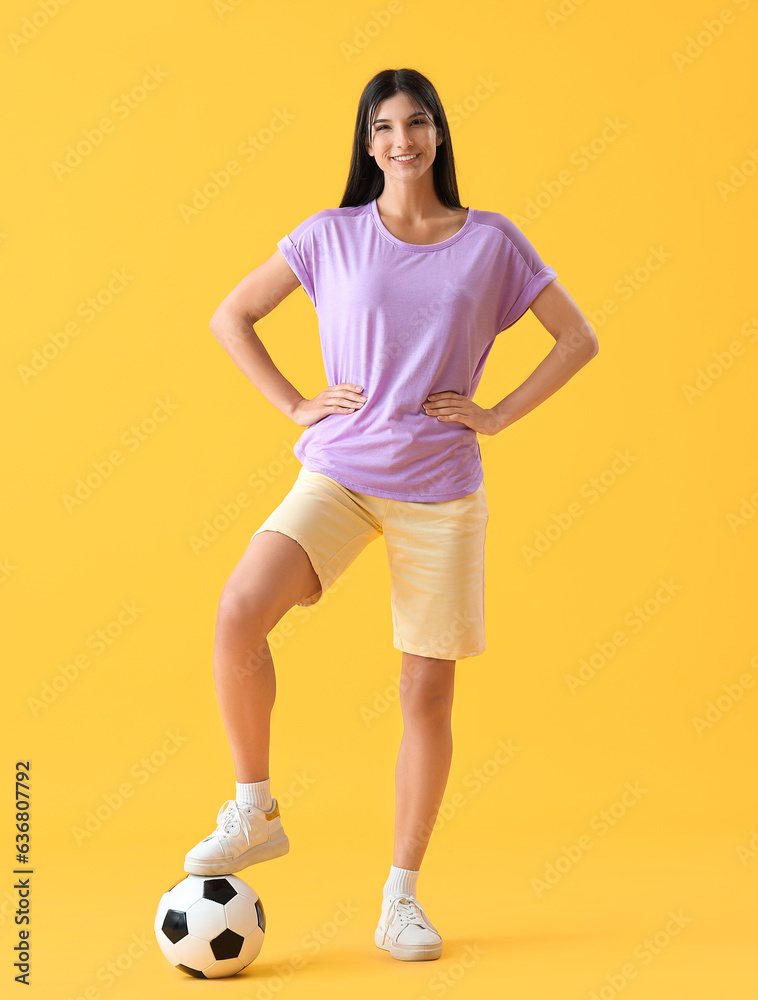 Young woman with soccer ball on yellow background