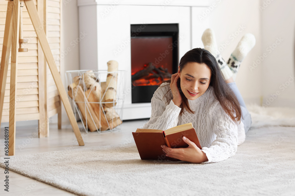 Young woman reading book near fireplace at home