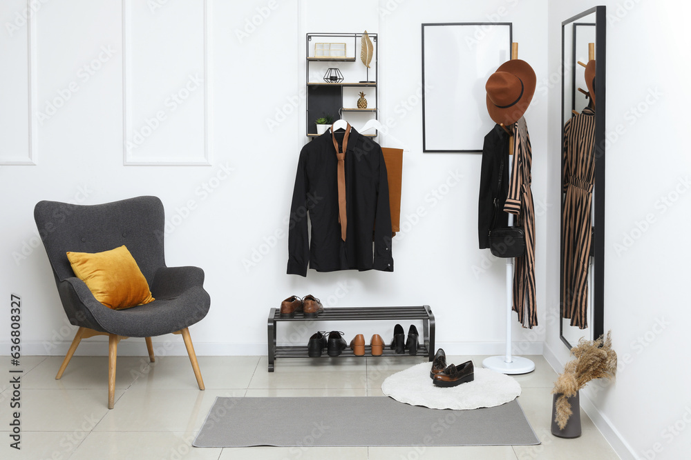 Interior of light hallway with mirror, rack and grey armchair