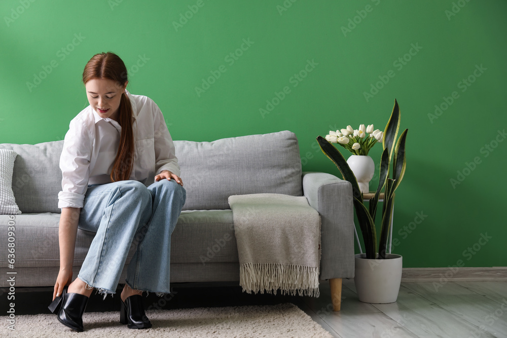 Young woman taking her shoes off at home after long working day