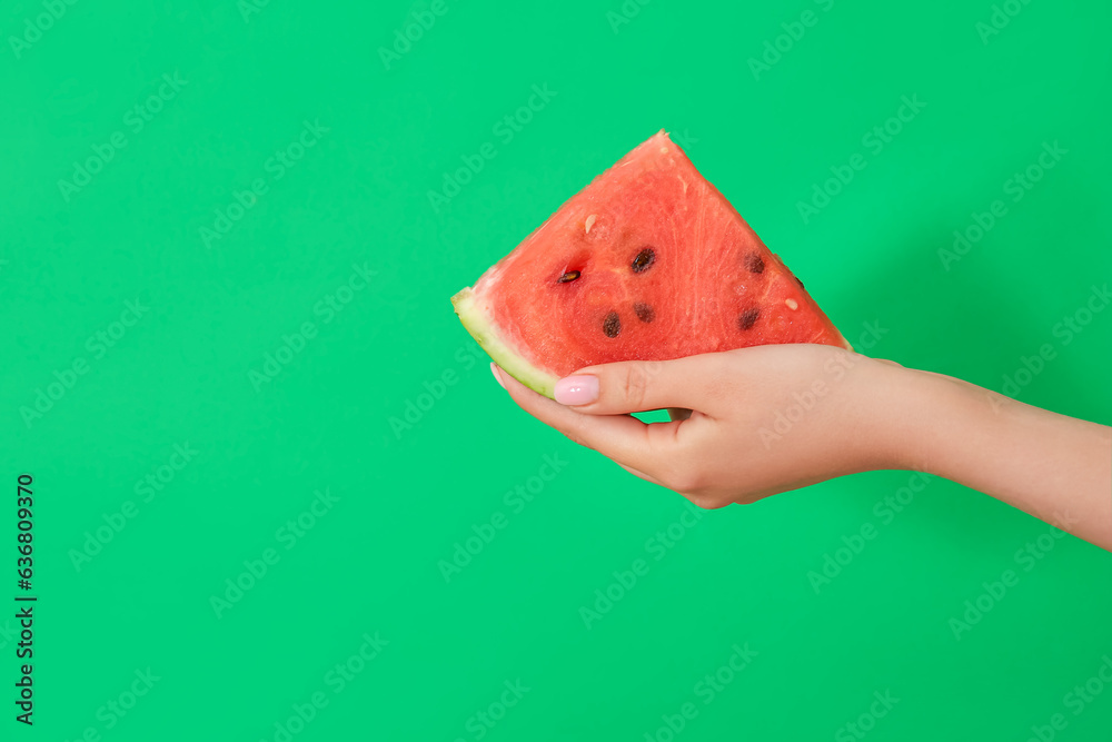 Female hand with piece of ripe watermelon on green background