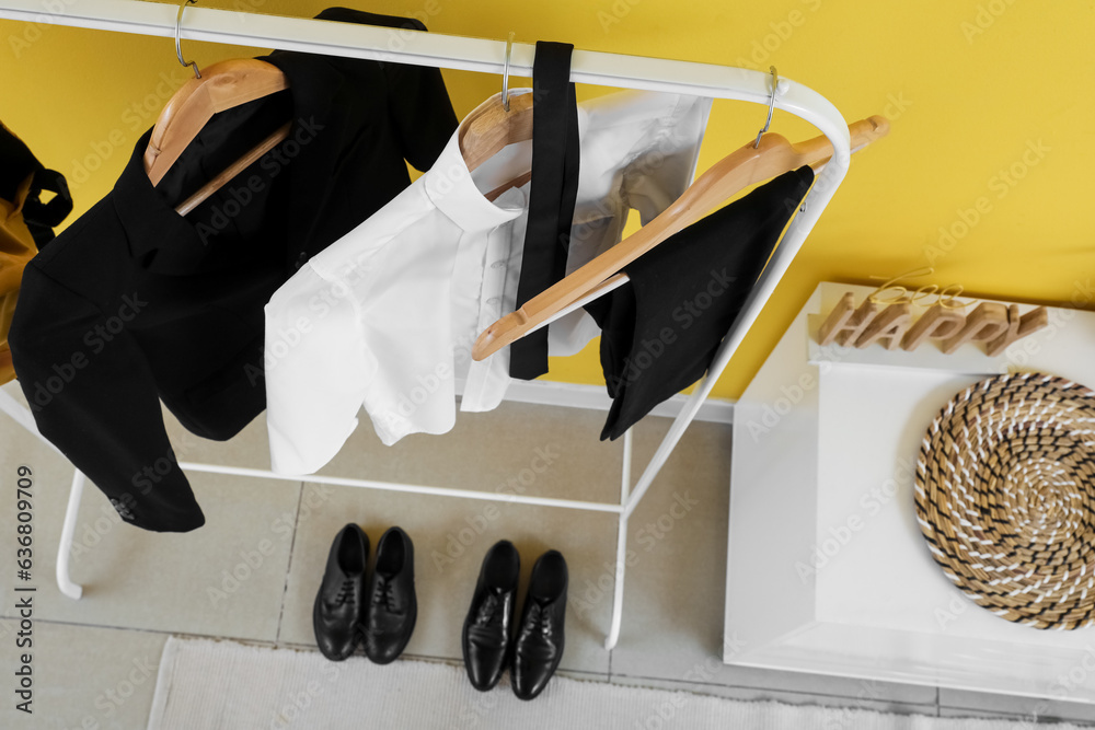 Rack with stylish school uniform near yellow wall in room