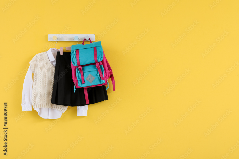 Stylish school uniform and backpack hanging on yellow background