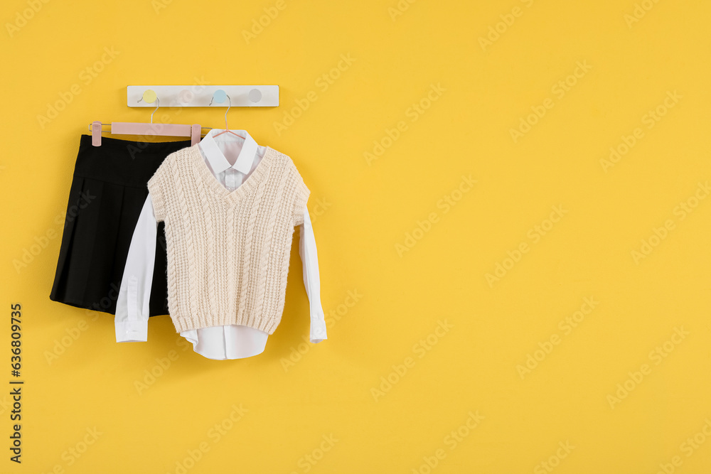 Stylish school uniform hanging on yellow wall