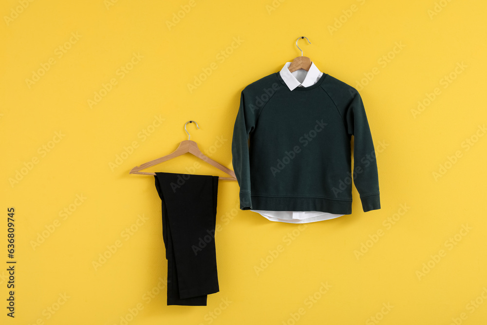 Stylish school uniform hanging on yellow wall