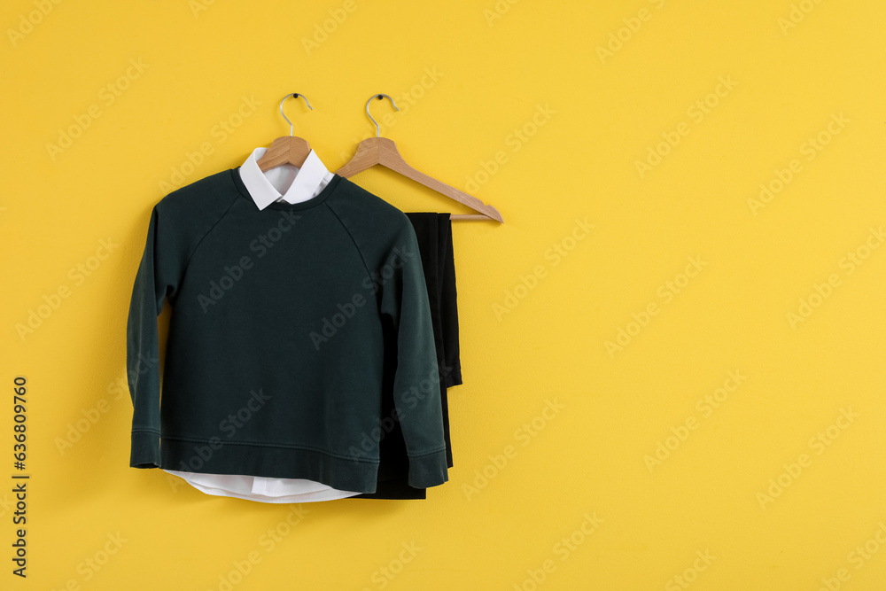 Stylish school uniform hanging on yellow wall