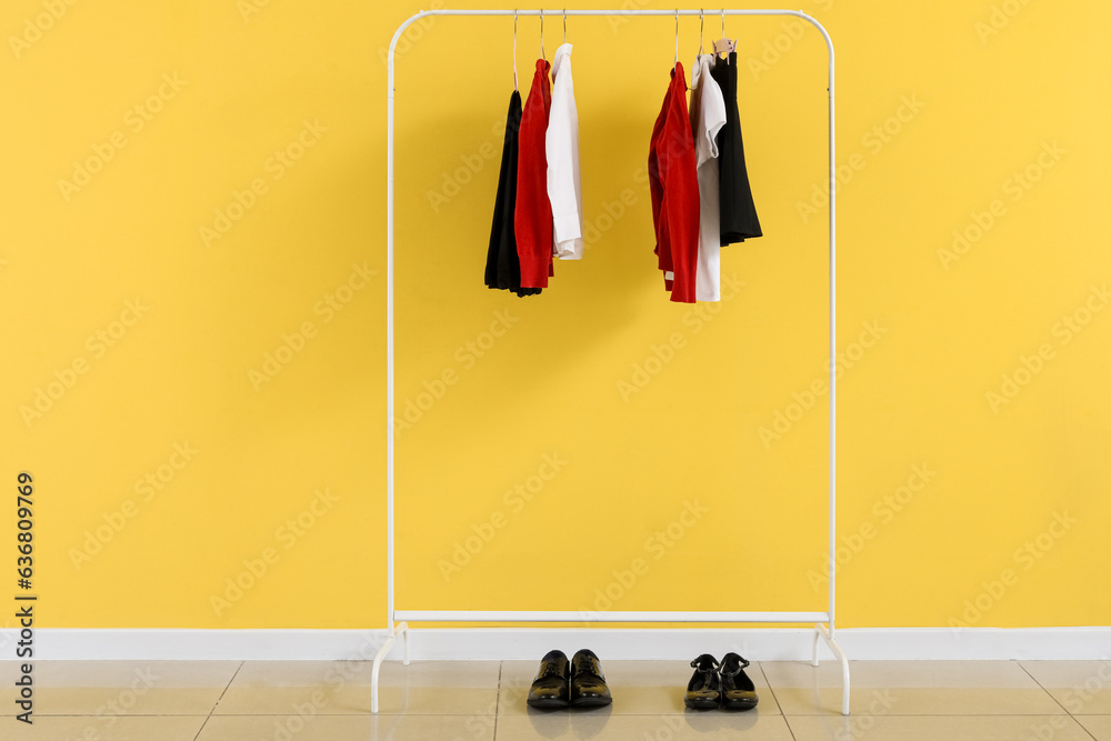 Rack with stylish school uniform near yellow wall in room