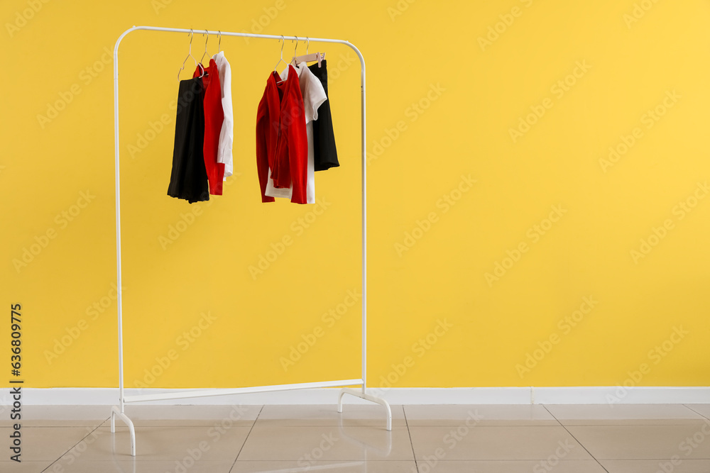 Rack with stylish school uniform near yellow wall in room