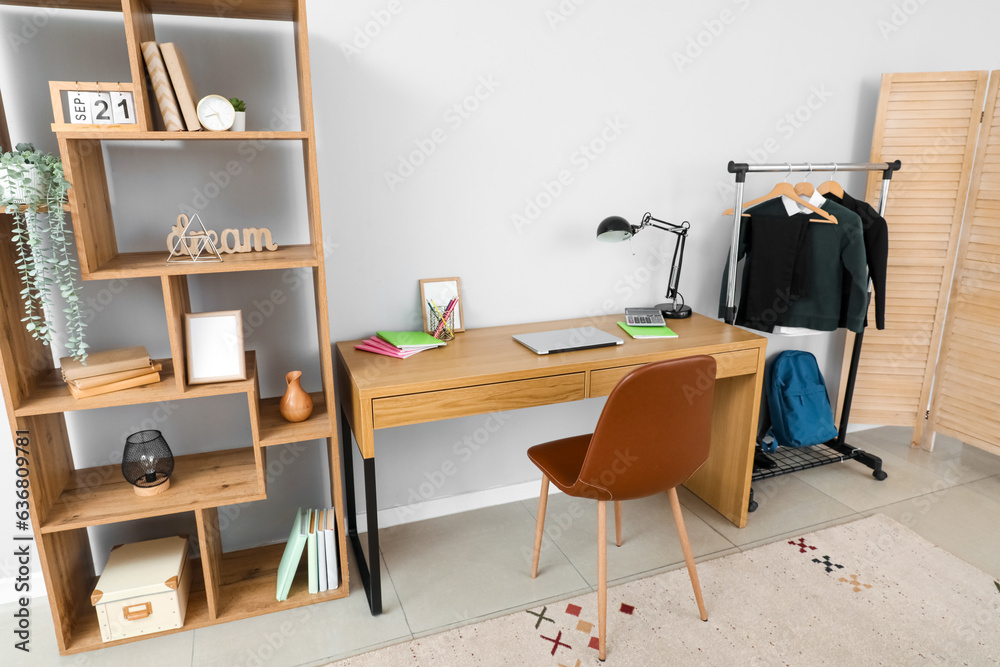 Interior of stylish room with modern workplace and school uniform on rack