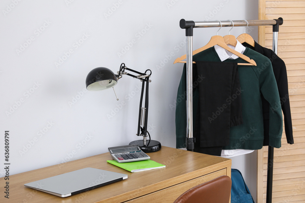 Interior of stylish room with modern workplace and school uniform on rack