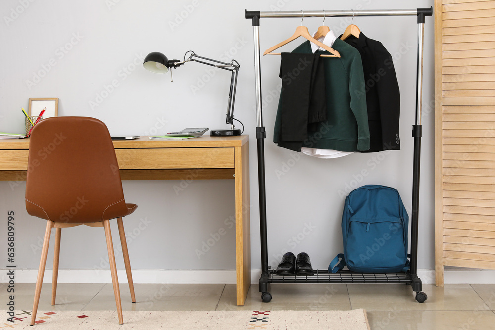 Interior of stylish room with modern workplace and school uniform on rack