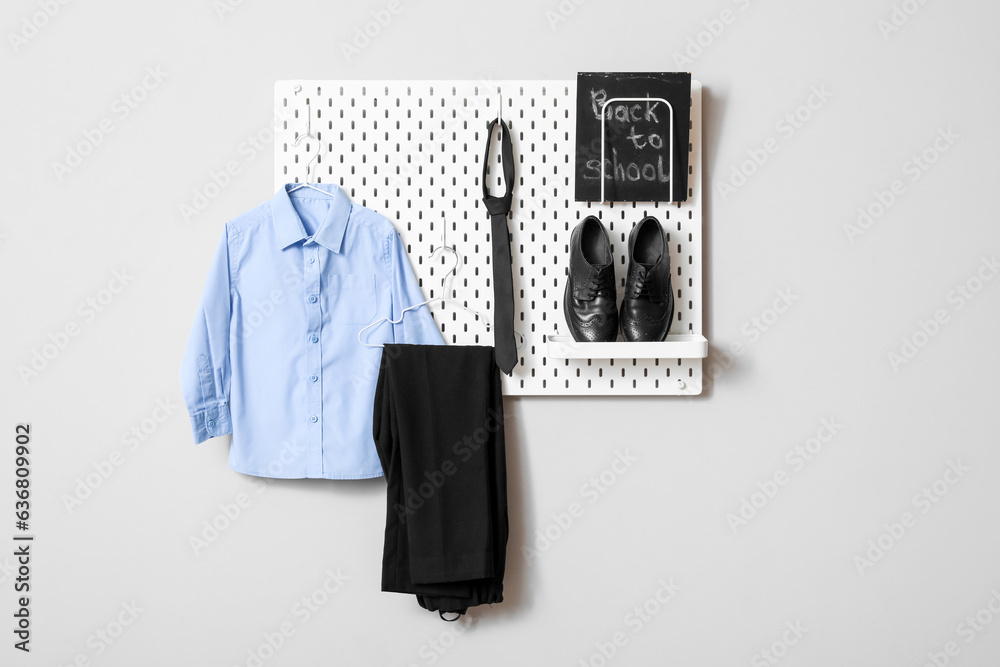 Stylish school uniform hanging on grey wall and blackboard with text BACK TO SCHOOL