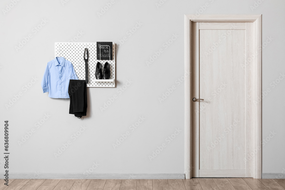 Stylish school uniform hanging on grey wall and blackboard with text BACK TO SCHOOL in room