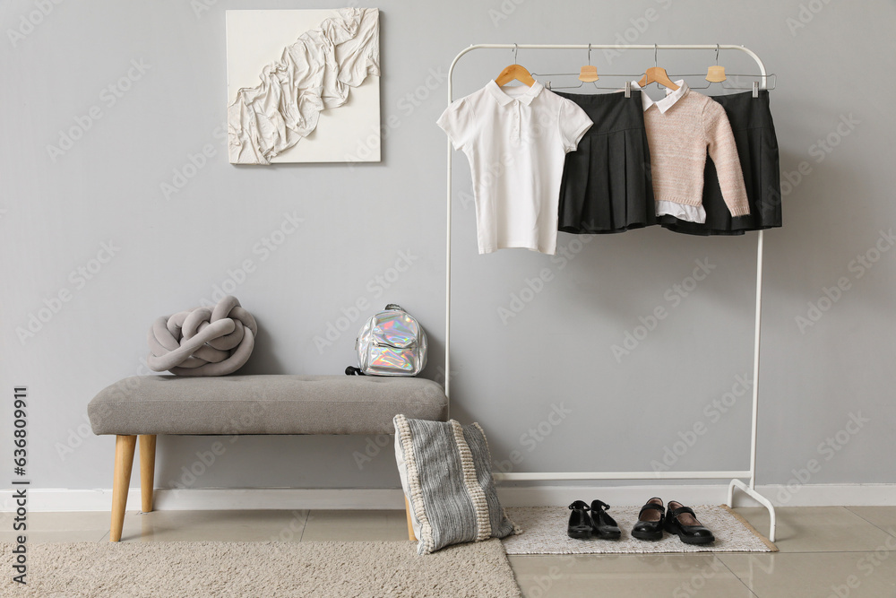 Rack with stylish school uniform near grey wall in room