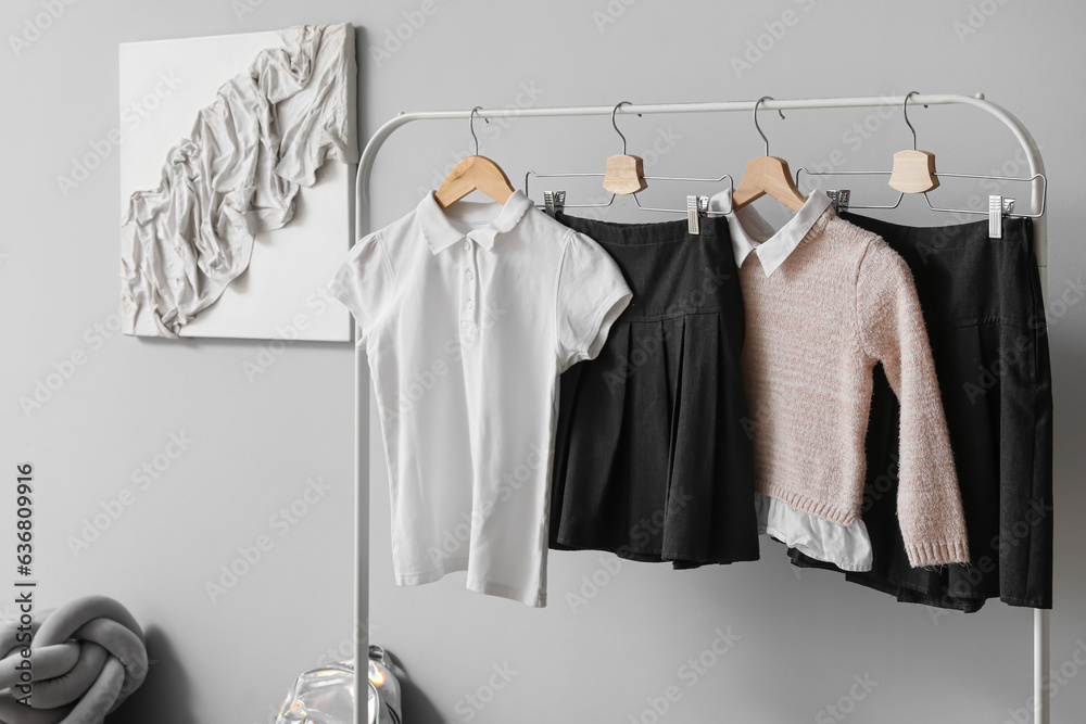 Rack with stylish school uniform near grey wall in room