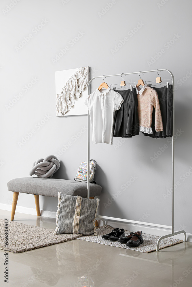 Rack with stylish school uniform near grey wall in room