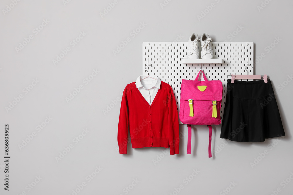 Stylish school uniform and backpack hanging on grey wall