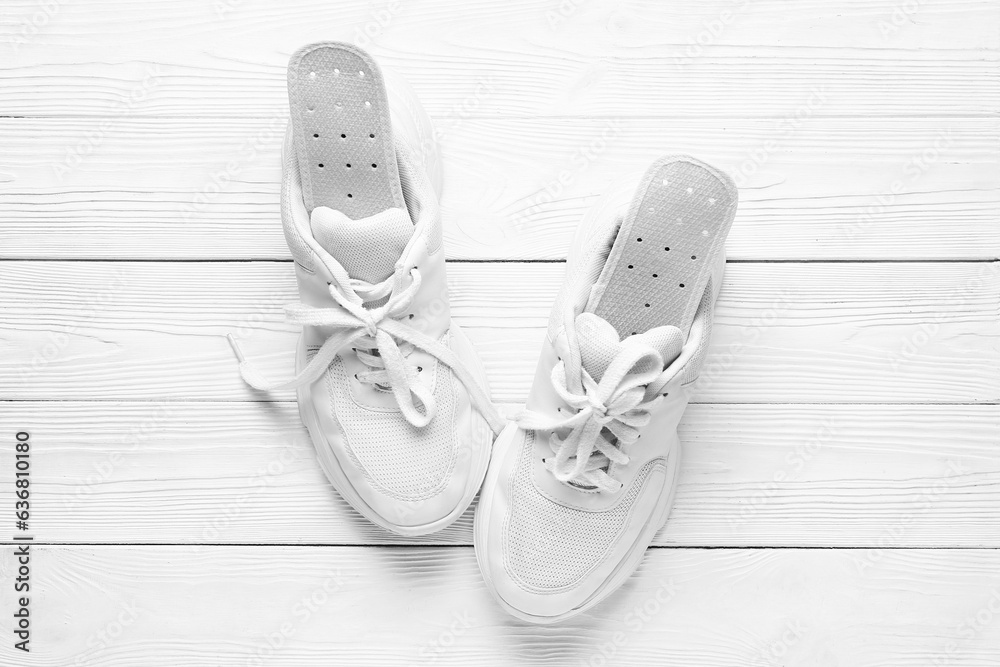 Pair of stylish sneakers with orthopedic insoles on light wooden background