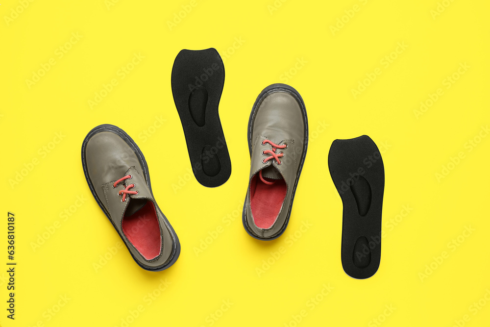 Pair of stylish shoes and orthopedic insoles on yellow background