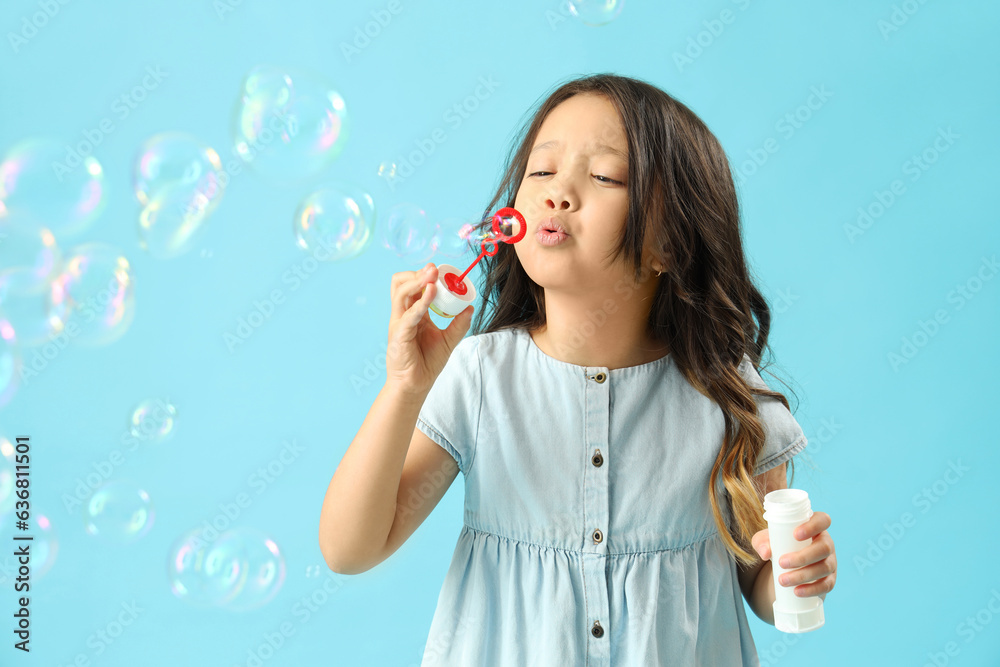 Cute little girl blowing soap bubbles on light blue background