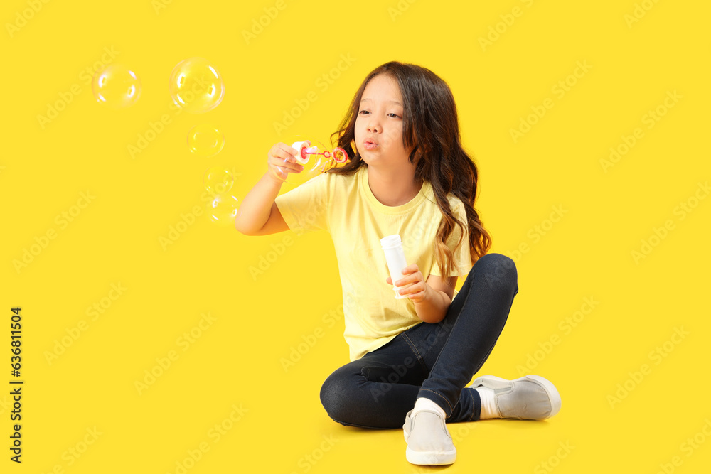 Cute little girl blowing soap bubbles on yellow background