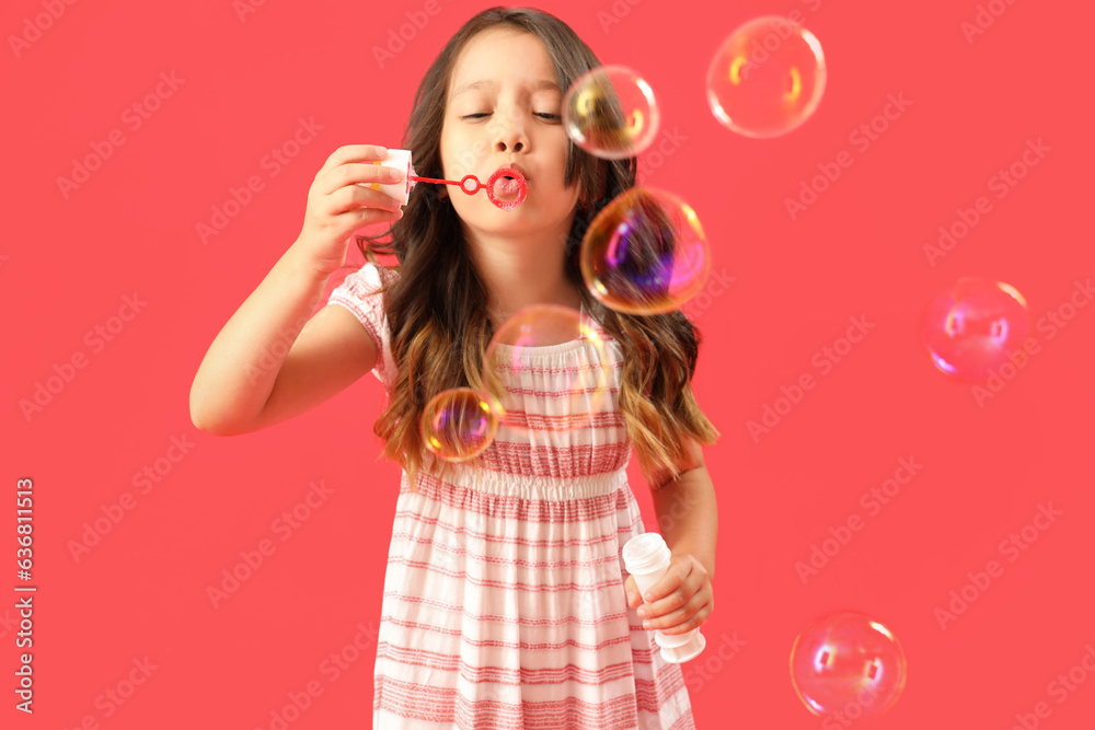 Cute little girl blowing soap bubbles on red background