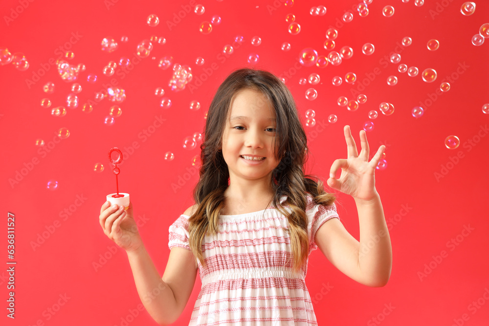 Cute little girl showing OK and soap bubbles on red background