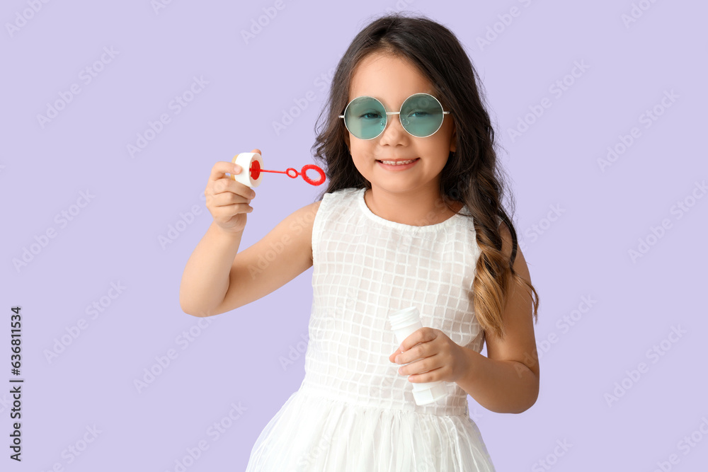 Cute little girl blowing soap bubbles on lilac background