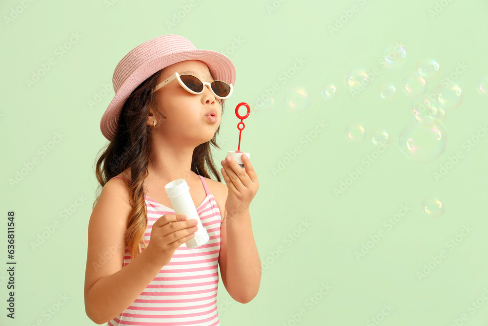 Cute little girl blowing soap bubbles on green background