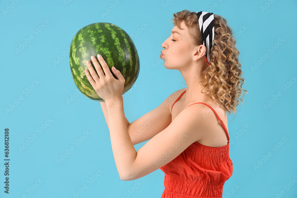 Beautiful young woman with ripe watermelon blowing kiss on blue background