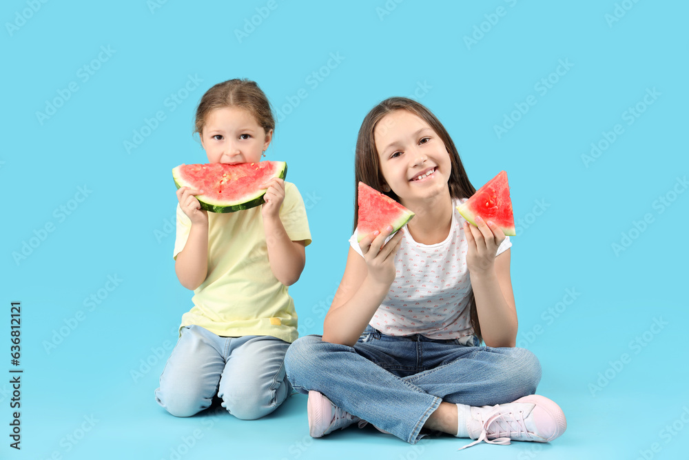 Little girls with slices of fresh watermelon sitting on blue background