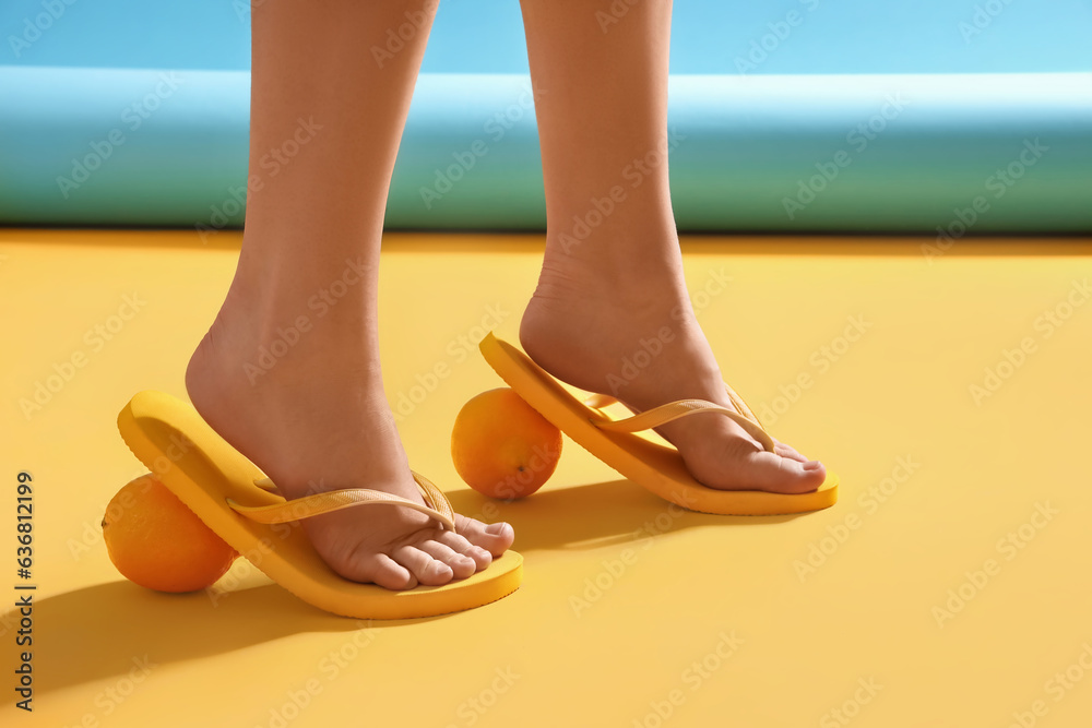 Female legs in stylish flip flops with citruses on color background