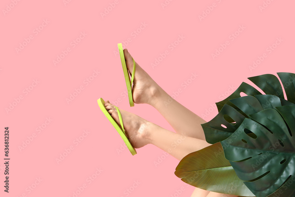 Female legs in stylish flip flops with palm leaves on pink background