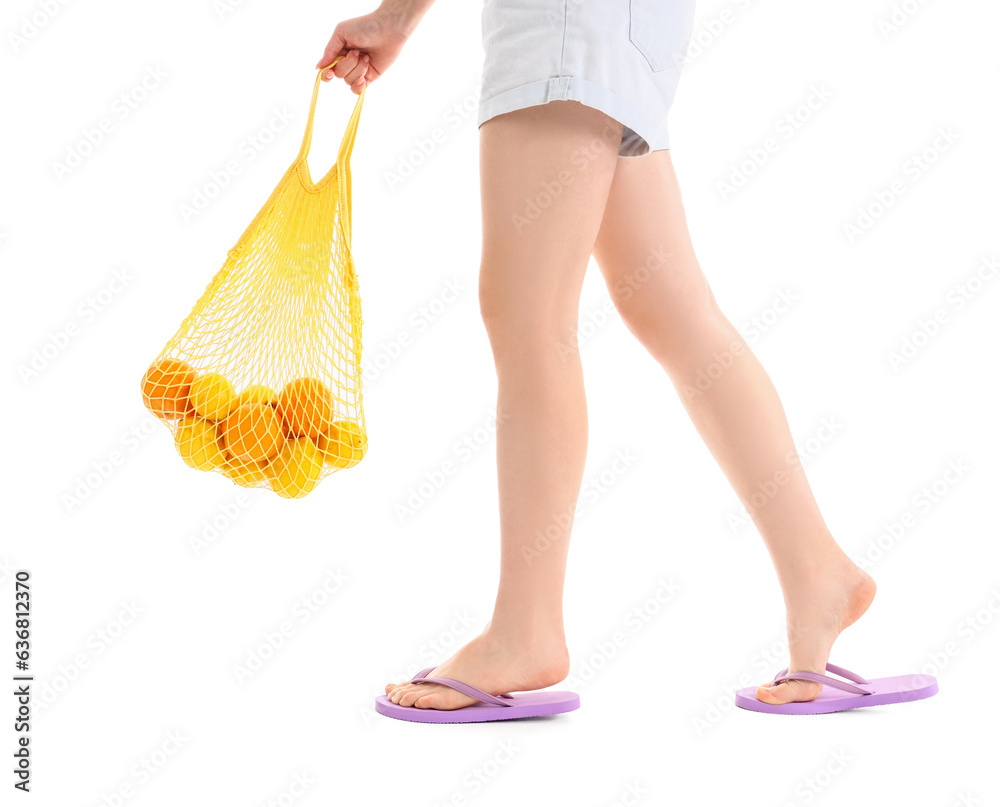 Female legs in stylish flip flops with string bag full of citruses isolated on white background