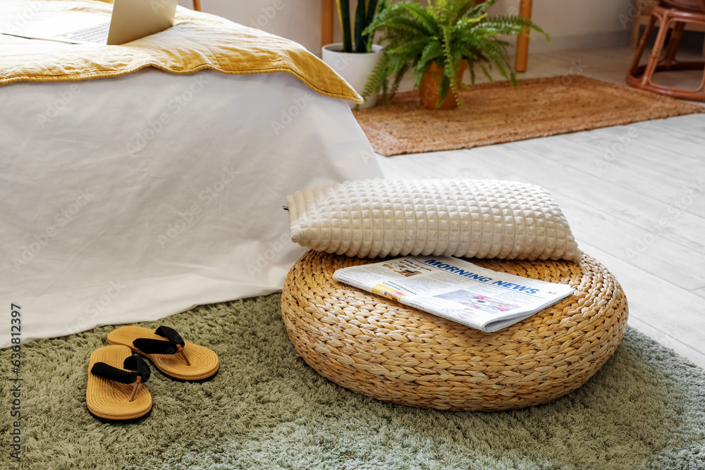 Rattan pouf with newspaper and flip flops in stylish bedroom