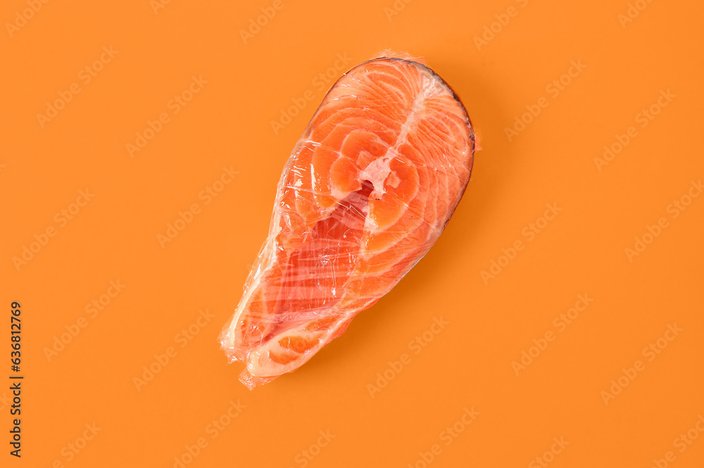 Fresh salmon steak in plastic food wrap on orange background