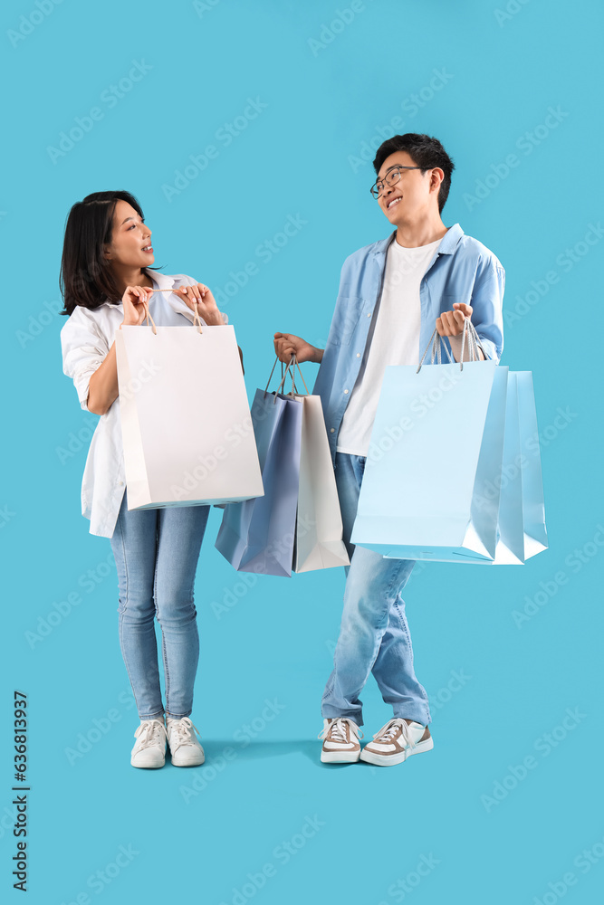 Young Asian friends with shopping bags on blue background