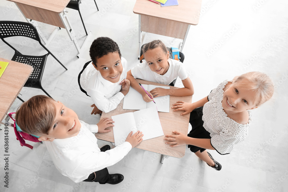 Little classmates writing at desk in classroom