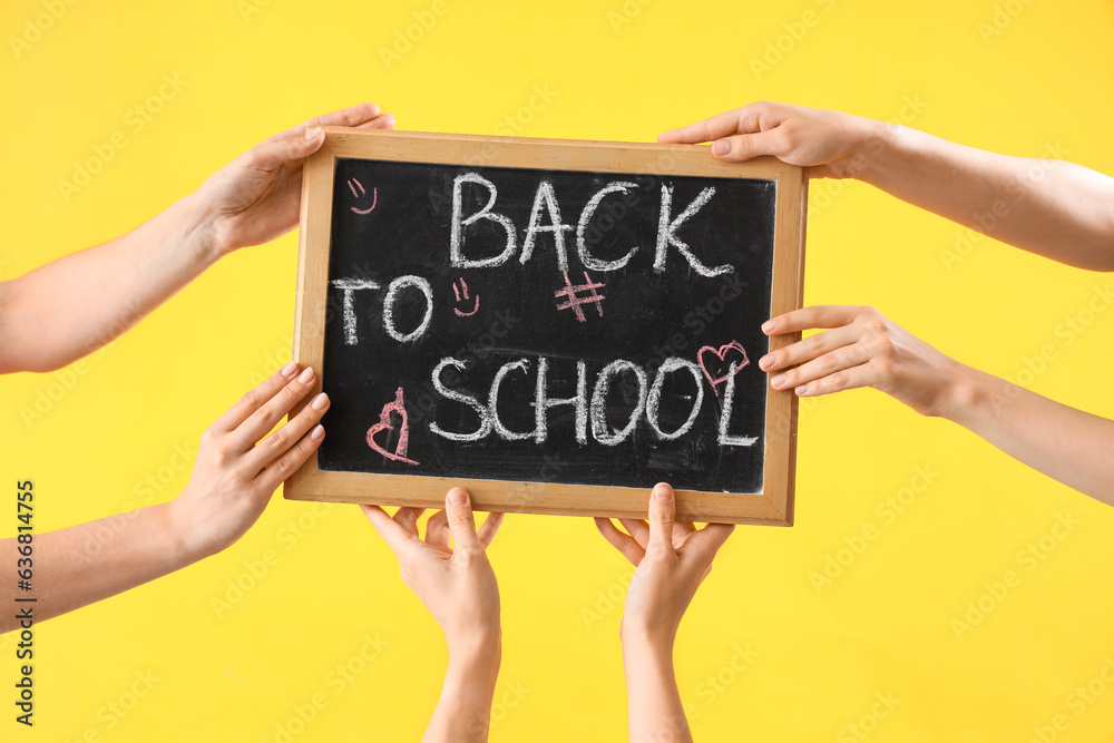 Many female hands holding blackboard with text BACK TO SCHOOL on yellow background