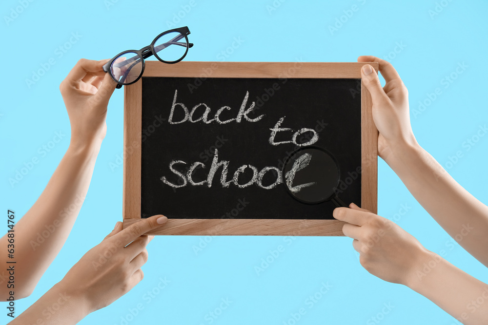 Female hands holding eyeglasses and blackboard with text BACK TO SCHOOL on blue background