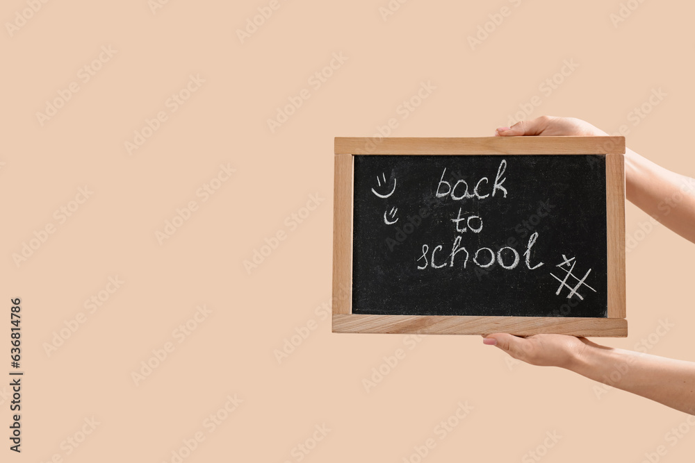 Female hands holding blackboard with text BACK TO SCHOOL on beige background