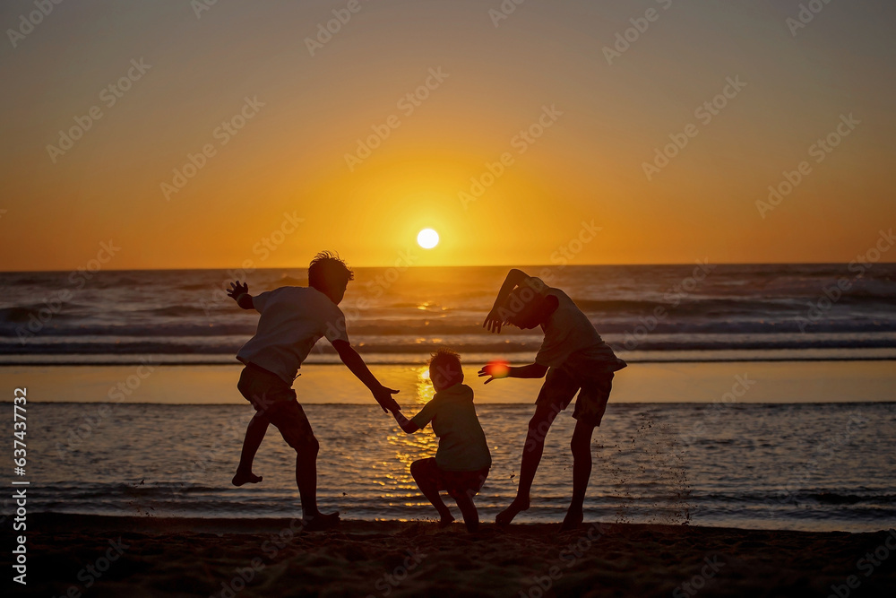 Happy children, boys, playing on the beach on sunset, kid cover in sand, smiling, laughing