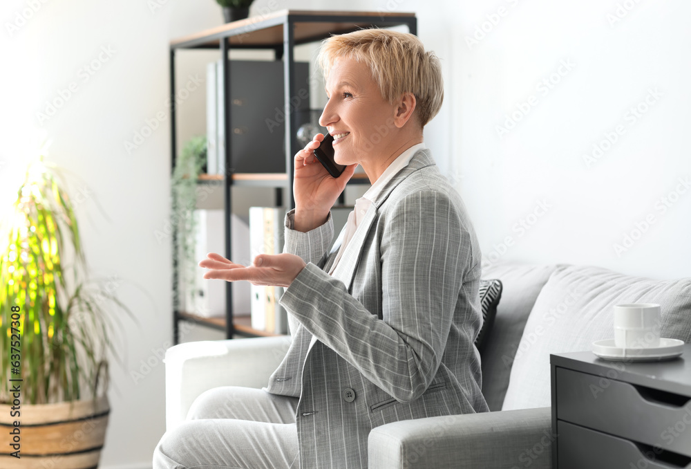 Mature businesswoman talking by phone while sitting on sofa in office